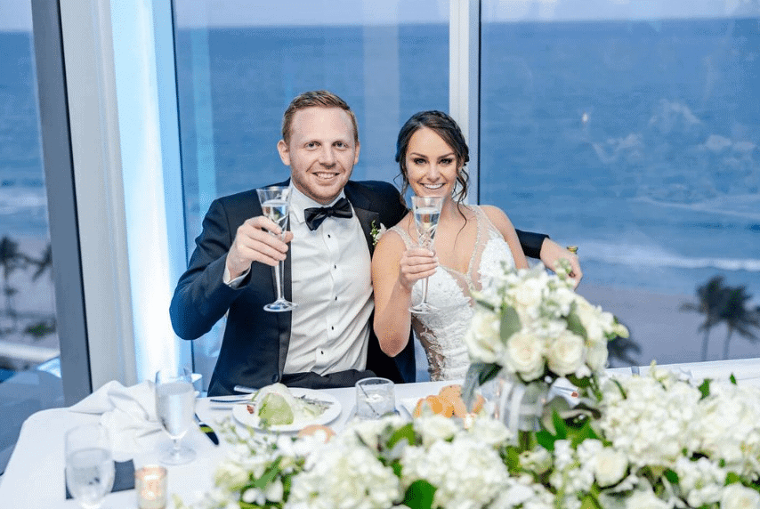 Bride and groom raising glasses with ocean view backdrop.