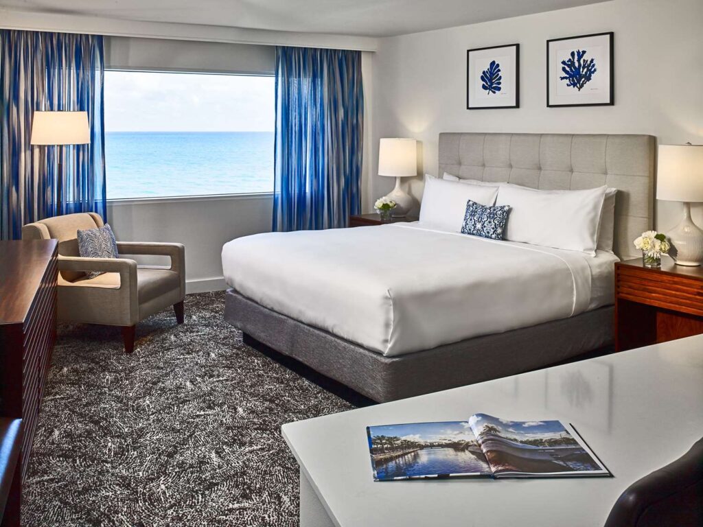 Hotel guestroom with a bed, seating area, working area, and an ocean view.