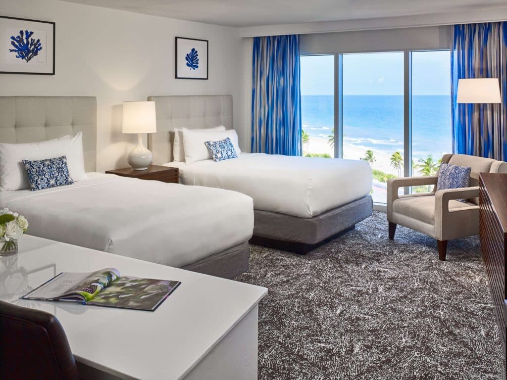 Hotel guestroom with two beds, seating area, working area, and a beach view.