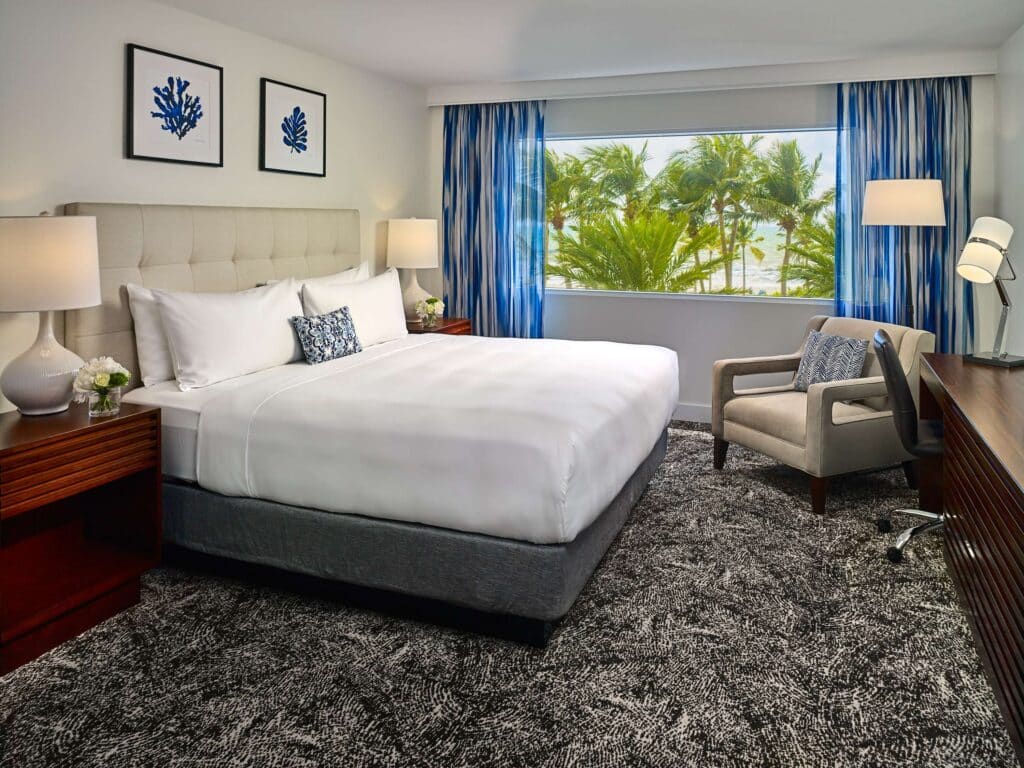 Hotel guestroom with a bed, seating area and a beach view.