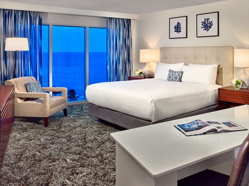 Hotel guestroom with a bed, seating area, working area, and an ocean view.