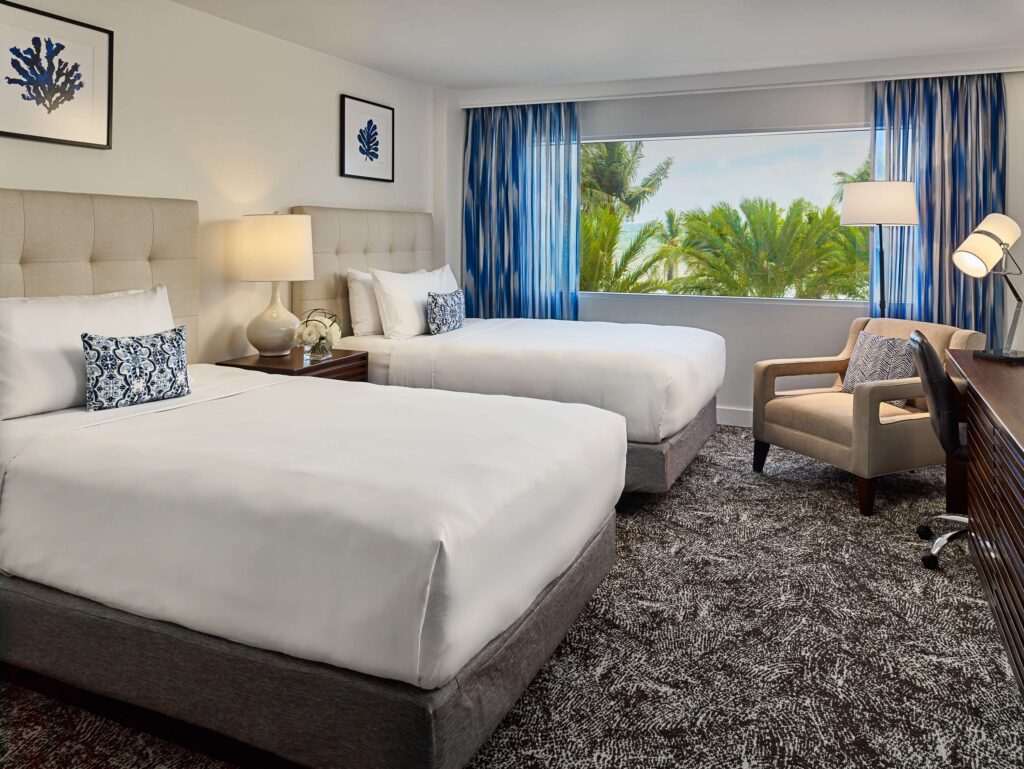 Hotel guestroom with two beds, seating area and a beach view.