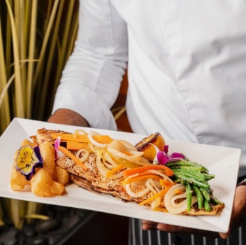 Chef presenting a plated seafood dish with vegetables.