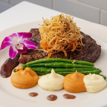 Steak dish garnished with vegetables and edible flower.