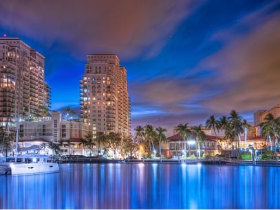 Nighttime cityscape with waterfront and illuminated buildings.