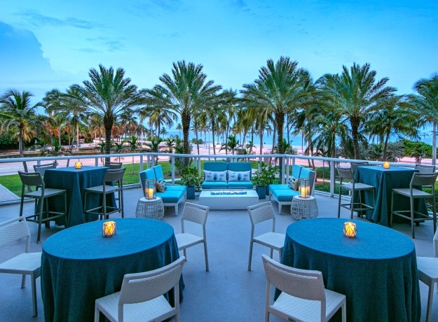 Outdoor event area with tables, candles, and palm trees.