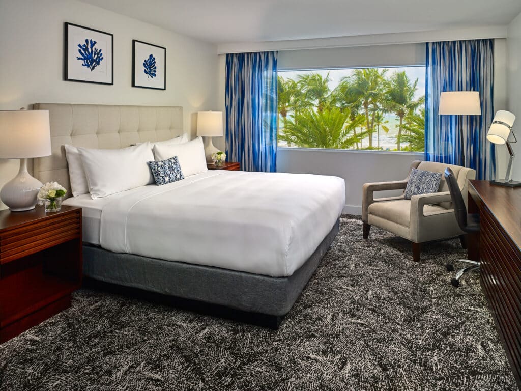 Hotel guestroom with a bed, seating area, working area, and a beach view.