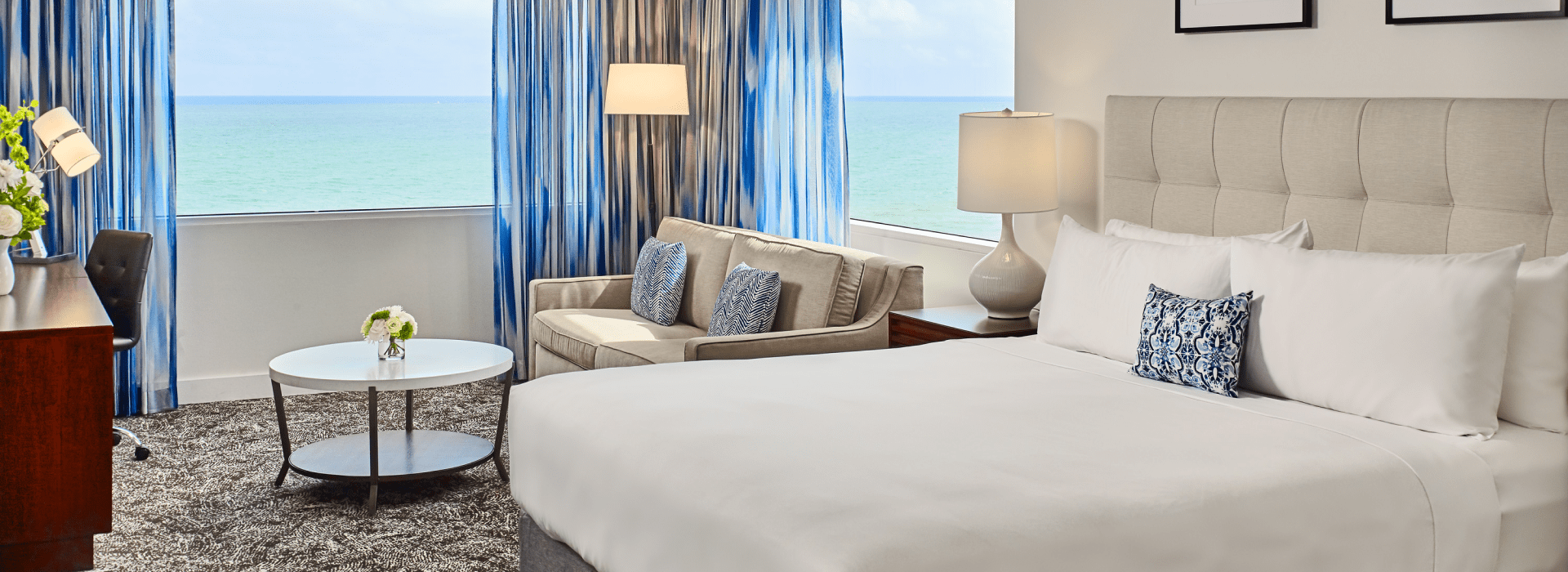 Hotel suite with an ocean view, bed and a seating area.