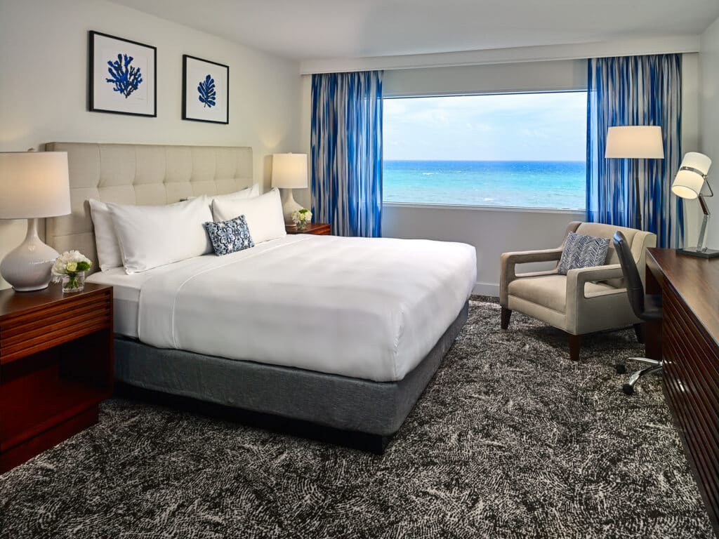 Hotel guestroom with a bed, seating area, and an ocean view.