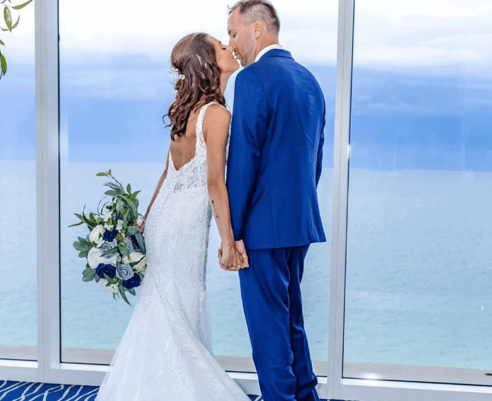 Bride and groom kissing by ocean view windows.