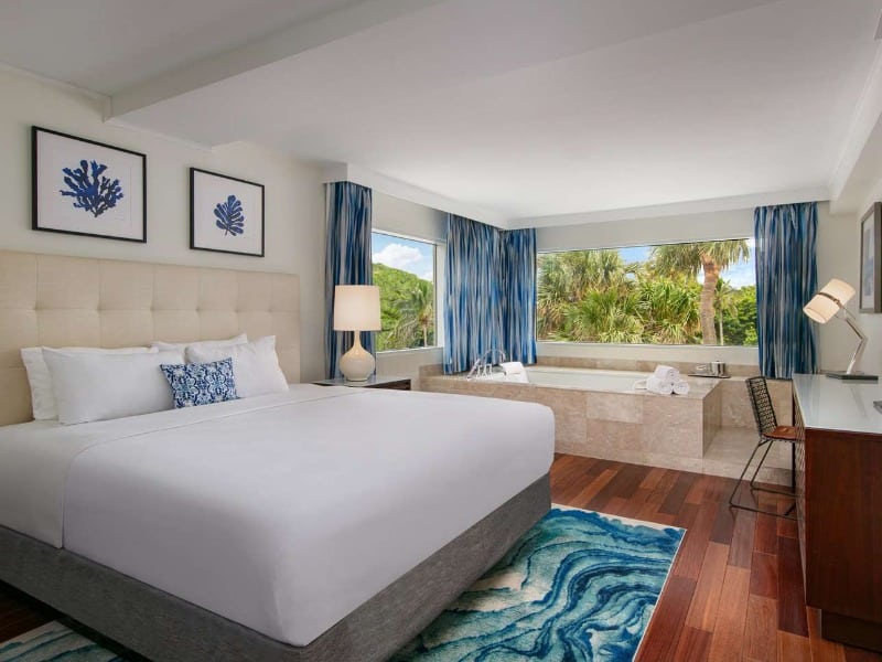 Hotel guestroom with a bed, bath, working area, and a beach view.