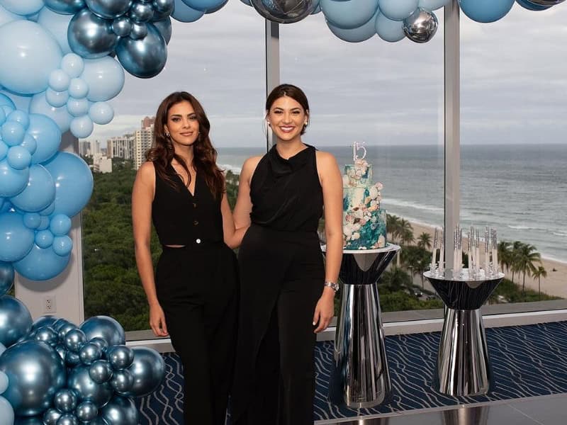 Two women posing by ocean view and blue balloon decor.