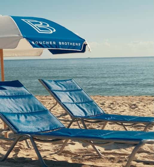 A blue and white beach umbrella and two beach lounge chairs on the beach.